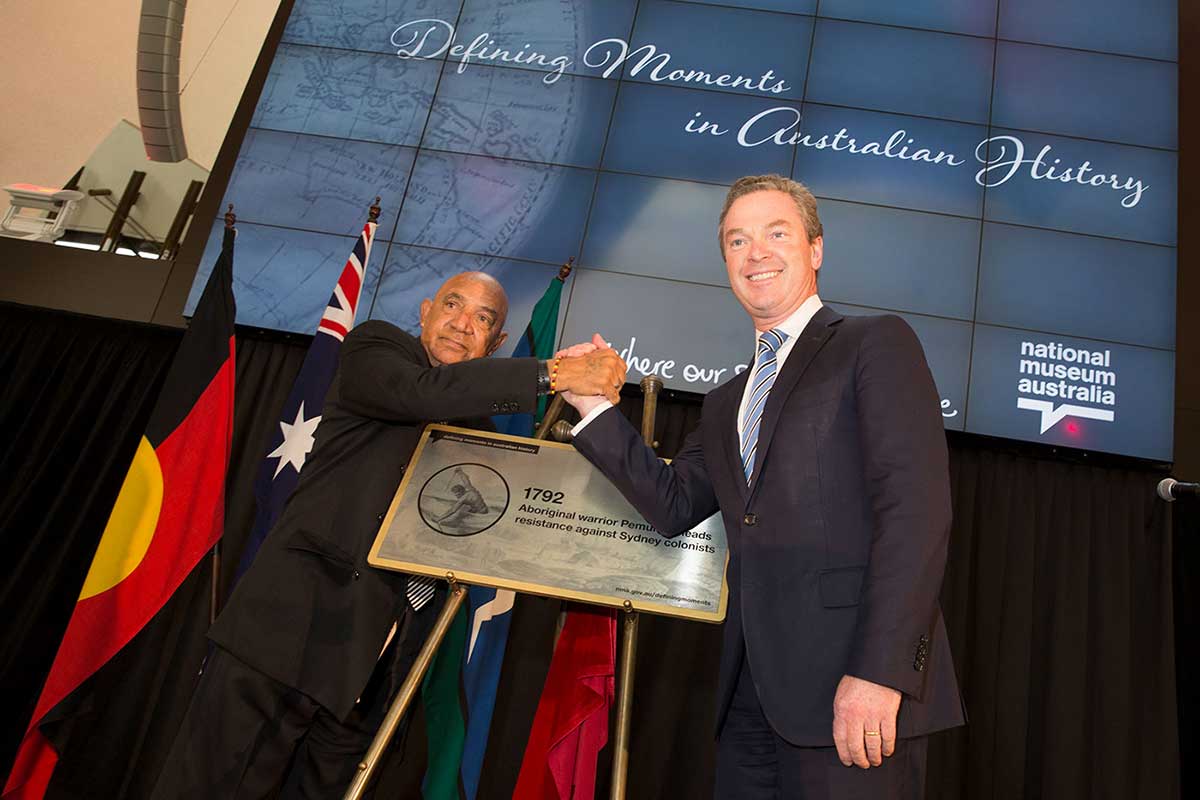Two men standing on a stage in front of a digital screen and shaking hands.