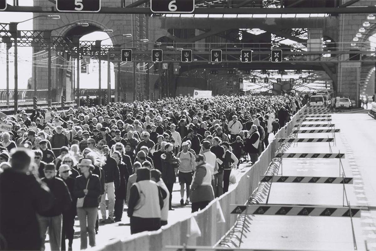 Black and white photo of a large crowd of people walking along the Sydney Harbour bridge.