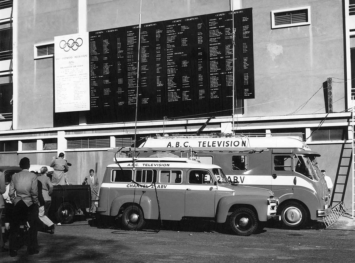 Two vans with ABC Television painted on their sides. They are parked next to a building with the Olympic rings on a board.