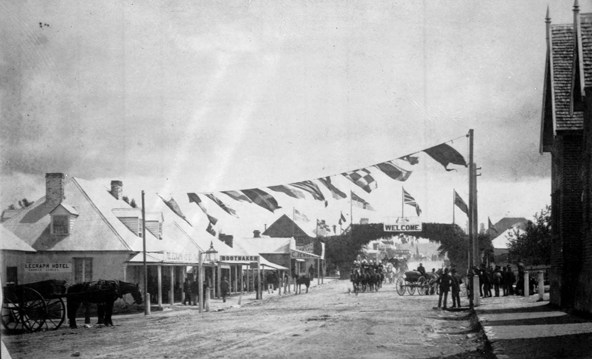 main street of small town with a horse and cart in foreground and a handful of people in the background. Bunting is suspended from poles