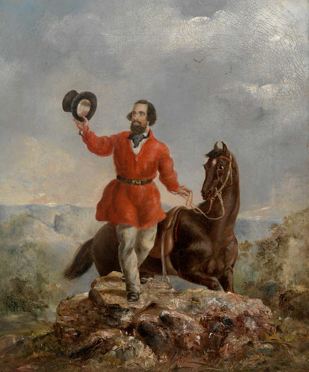 A bearded man wearing a bright red jacket and holding his top aloft stands on a rocky outcrop holding the reins of his horse. - click to view larger image