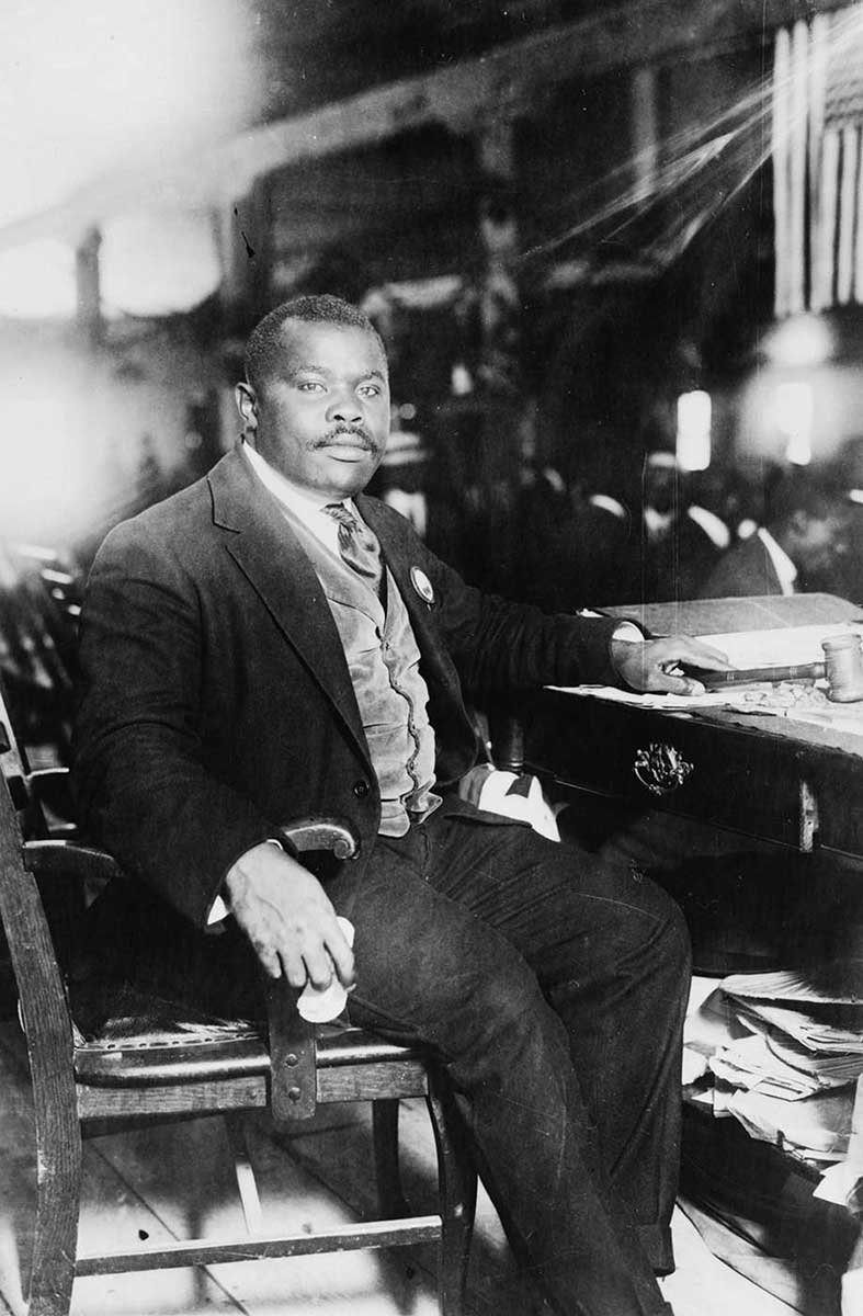 African man in a three-piece suit seated at a desk, looking at the camera. - click to view larger image