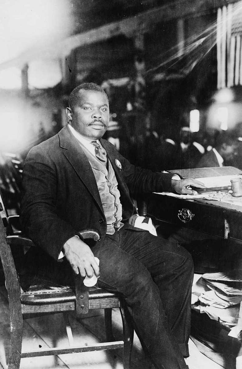 African man in a three-piece suit seated at a desk, looking at the camera - click to view larger image