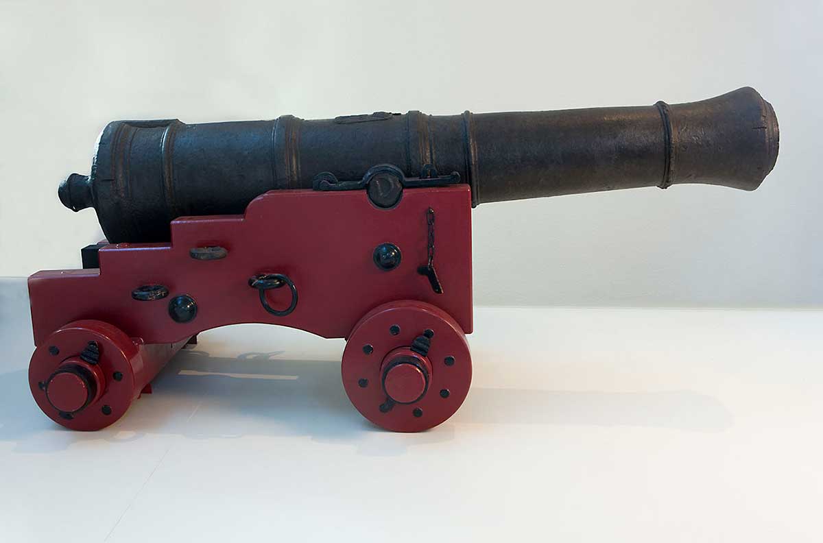 A cannon set on a replica wooden carriage constructed of unknown timbers with metal fittings painted red and black.