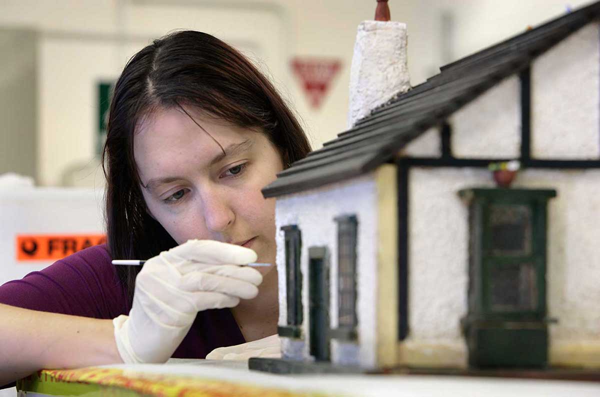Museum conservator applying an adhesive to the outside walls of the doll's house.
