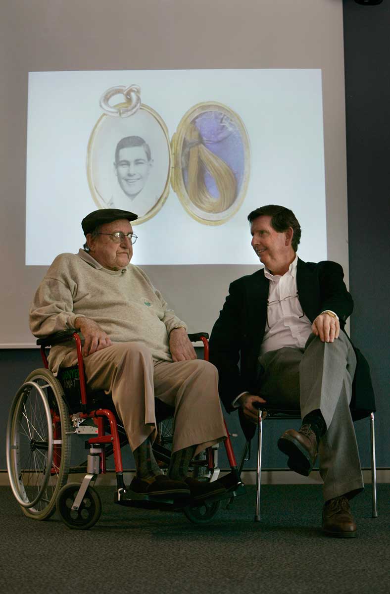 Kevin and John Hannan seated in front of large projected image of a locket with a photo of Les Darcy in it. - click to view larger image