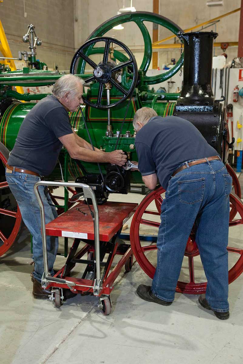 A colour photograph of two men working on a large steam engine. - click to view larger image