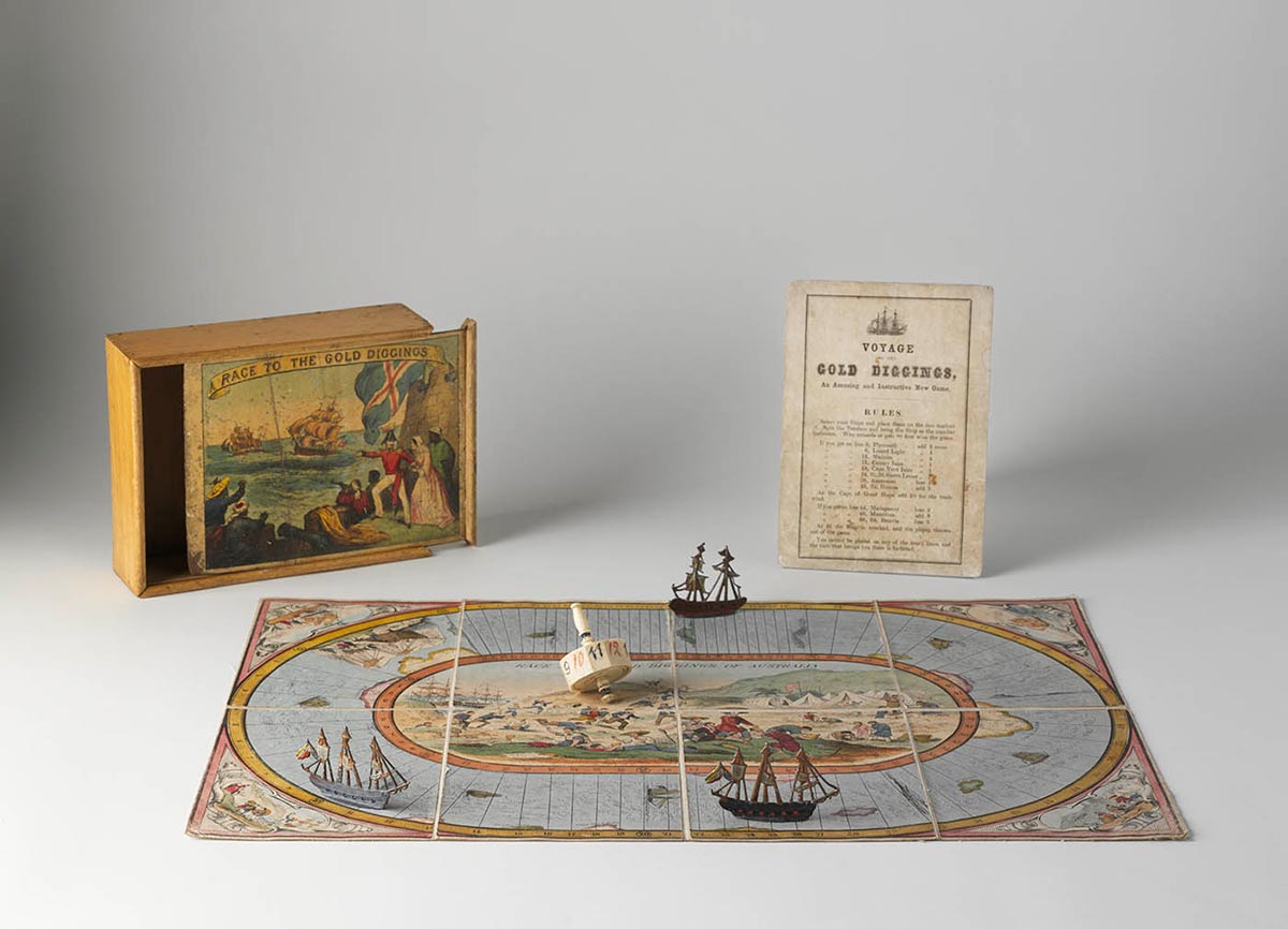 A hand-coloured lithographic playing board made of eight paper sections mounted on linen, with a polygonal twelve-sided teetotum or spinning dice and three small painted metal playing pieces in the shape of tall ships. A varnished wooden box and a instruction sheet have been placed beside the game board.