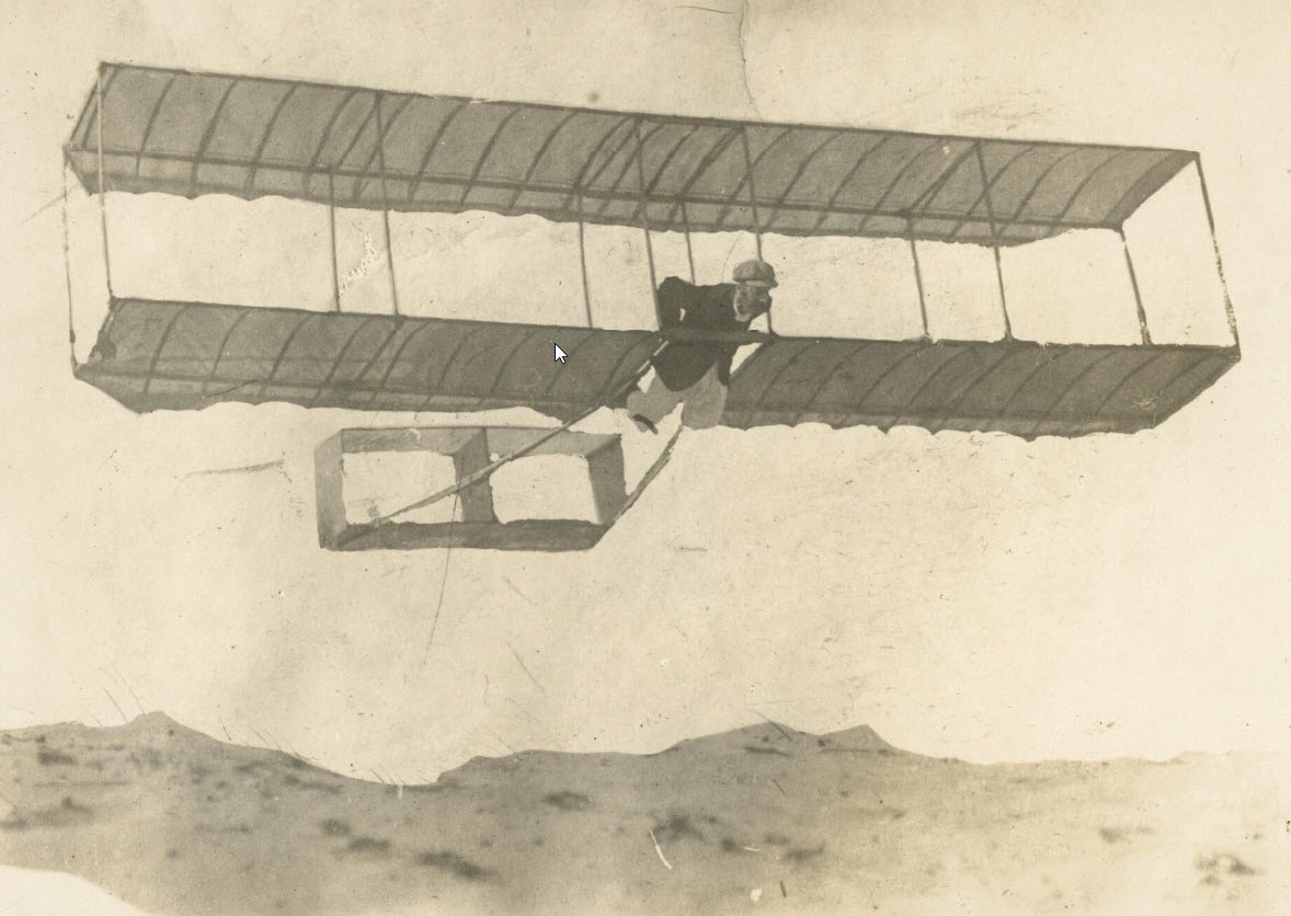 A biplane glider being flown above a sand dune.