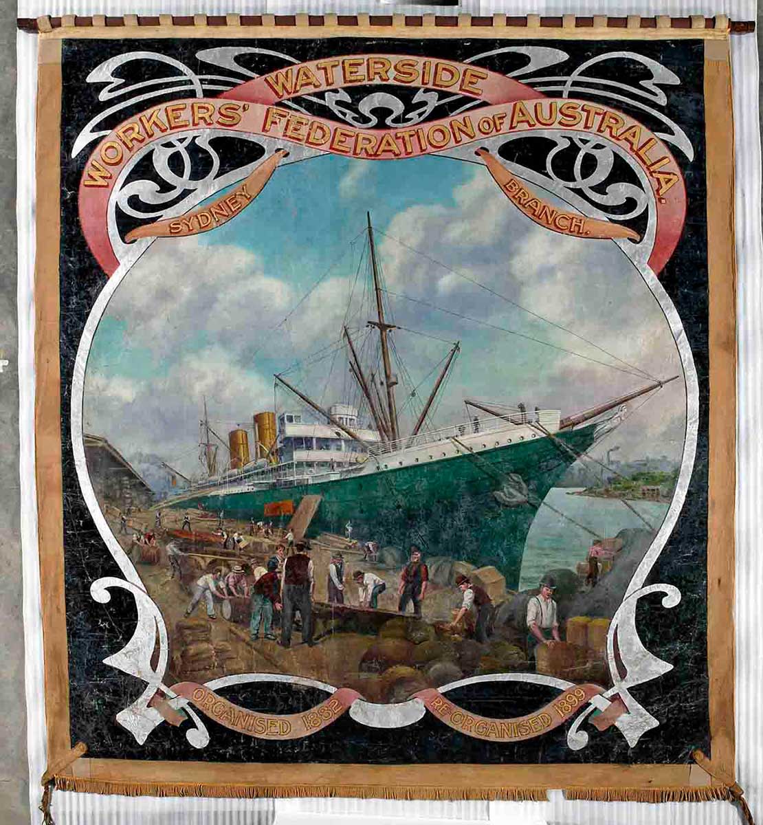Large almost square banner painted in oil colours, showing a central image of a ship docked beside a busy wharf. 'Waterside Workers' Federation of Australia' and 'Sydney branch' is written at the top. At the bottom the text reads 'Organised 1882', 'Re-organised 1899'. - click to view larger image