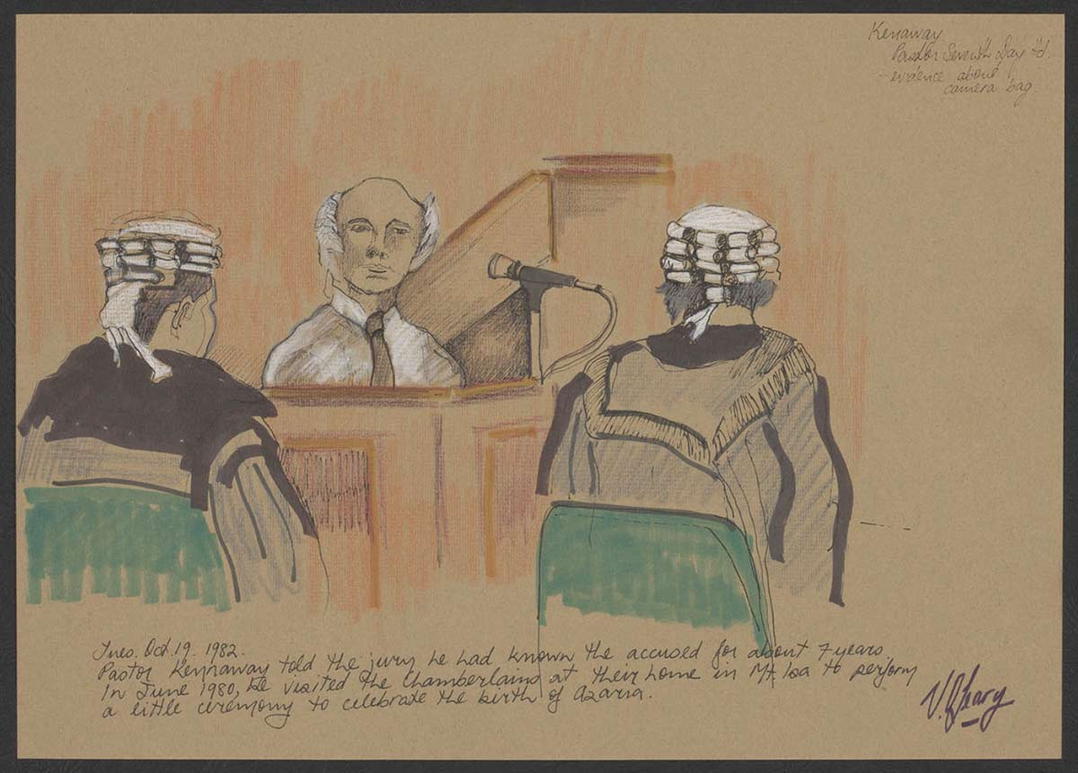 A man dressed in a white shirt and dark tie sits giving evidence in a courtroom. Two men in wigs and dark legal robes sit either side of him, facing the man. - click to view larger image