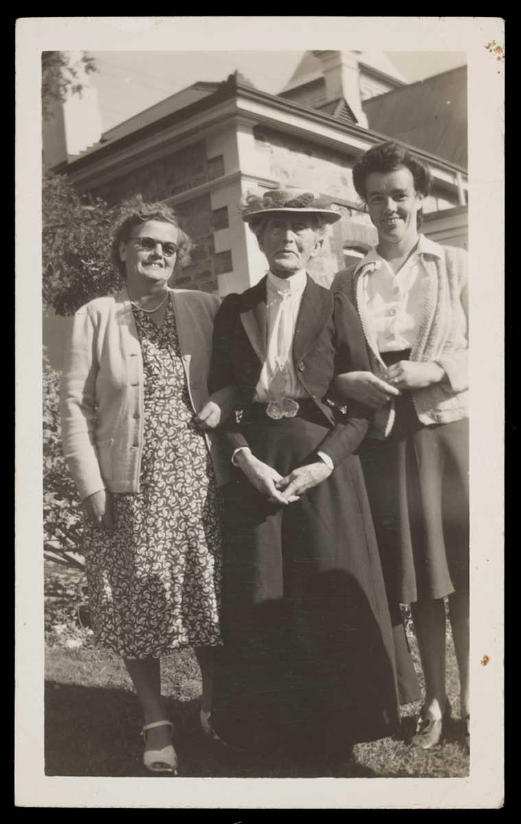 Black and white photograph showing three women standing in a garden. The woman at centre is older and wears Victorian dress. - click to view larger image