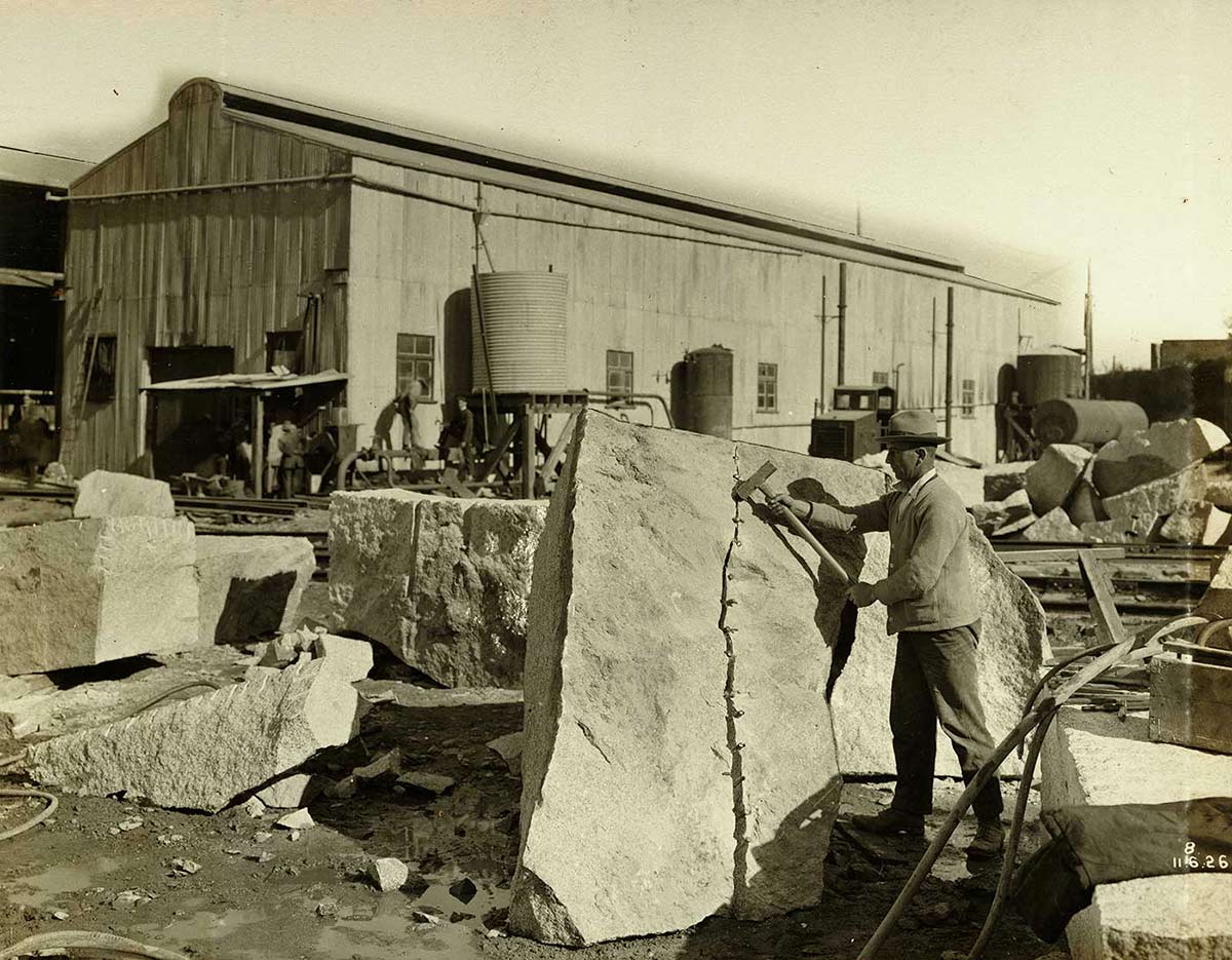 A worker uses wedges and a hammer to split a granite block. - click to view larger image