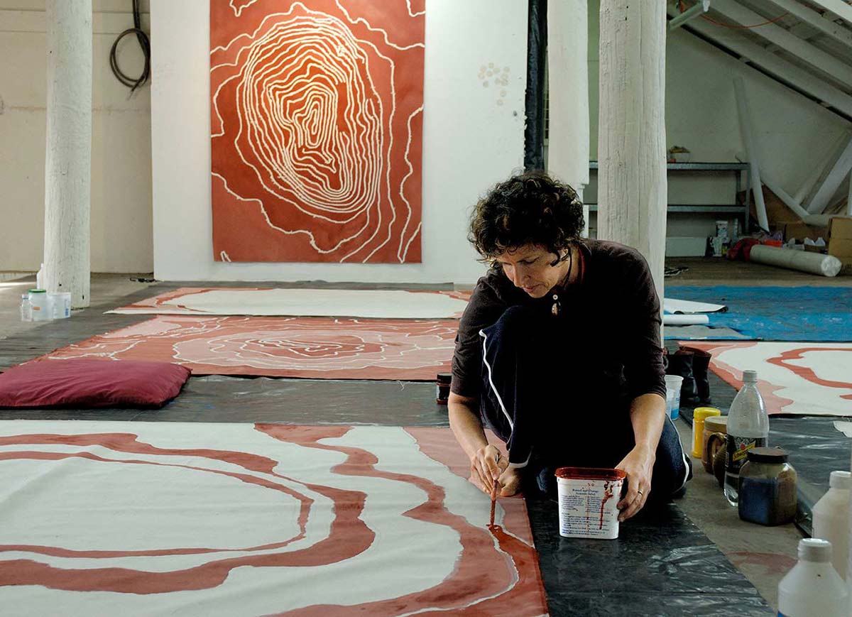 Judy Watson in her studio painting on the ground. - click to view larger image