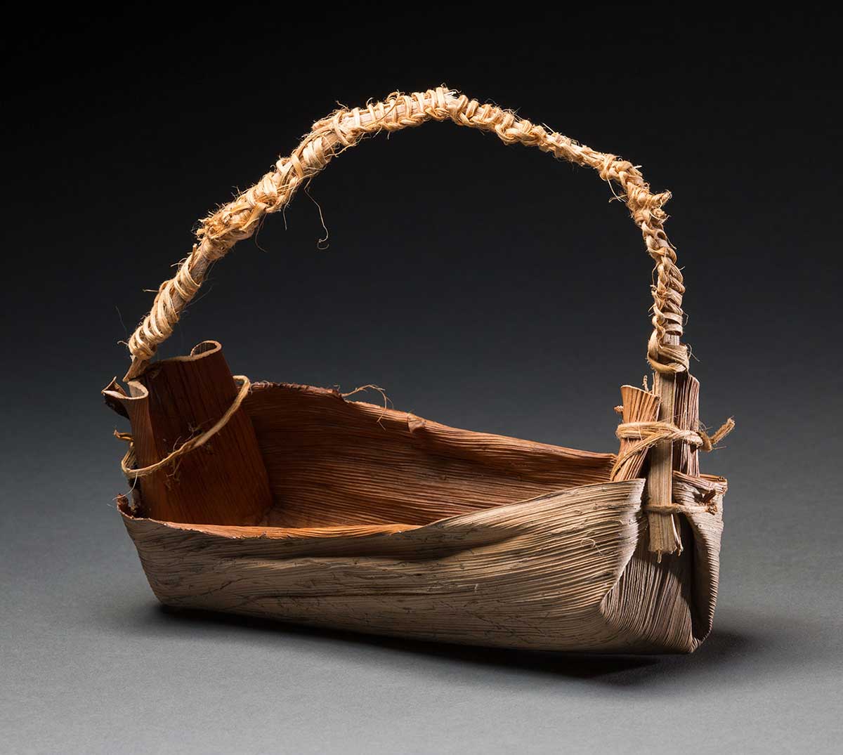 A rectangular shaped basket with a handle made of natural fibres. The handle has other natural fibres beige in colour wound around it.
