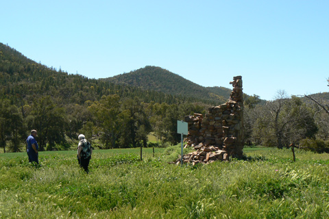 Remains of a stone structure in the centre of a green field, with hills in the background. - click to view larger image