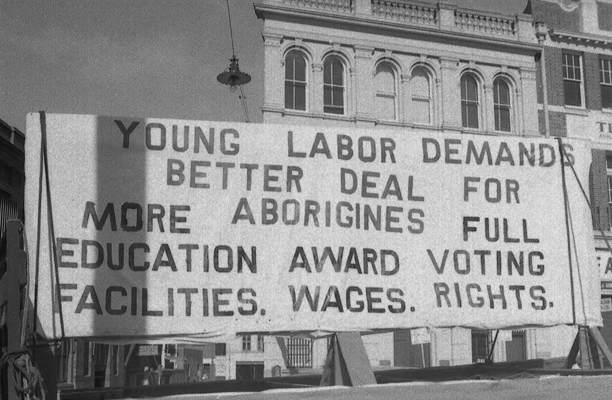 Black and white photo of a protest banner with text including: YOUNG LABOR DEMANDS BETTER DEAL FOR MORE ABORIGINES.