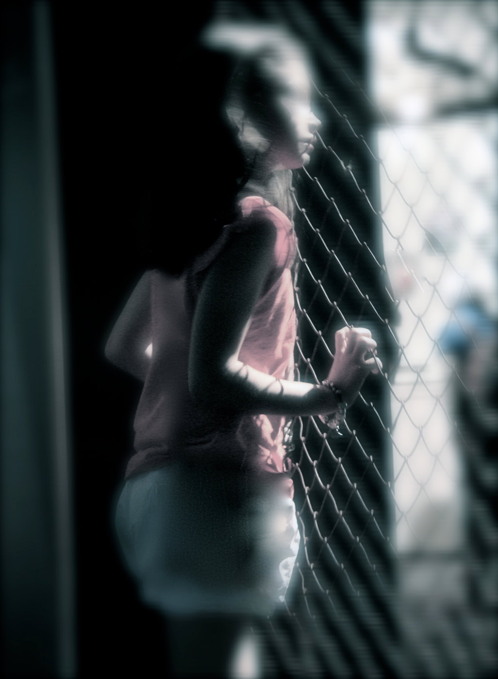 Blurred colour photograph showing a side view of a young girl looking through a wire mesh fence. - click to view larger image