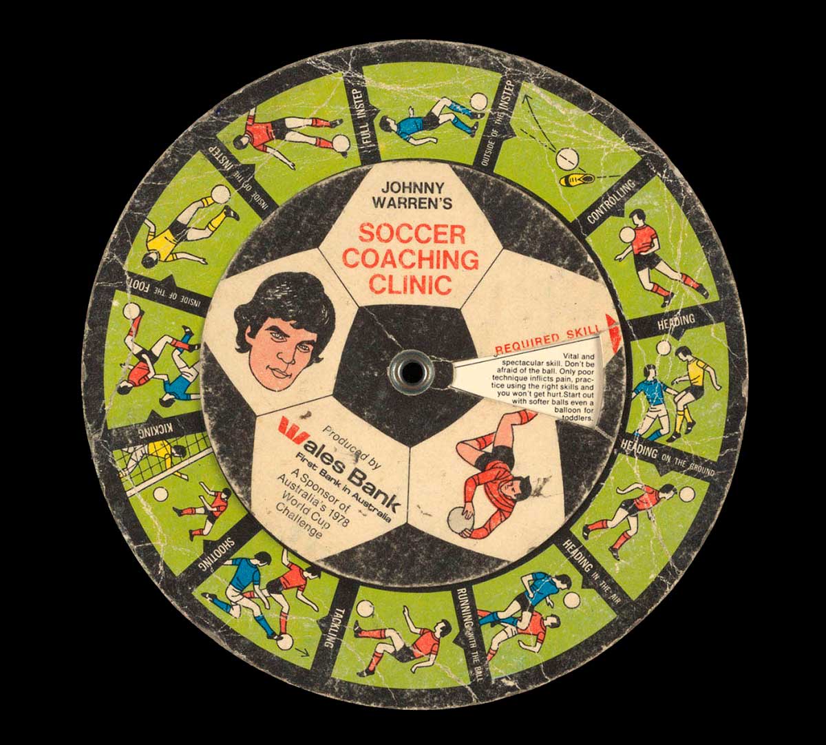 A colour printed cardboard disc with illustrations of football players in different positions, and accompanying descriptive text. There is an illustrated portrait of John Warren at the centre with text 'JOHNNY / WARREN'S SOCCER / COACHING / CLINIC / Produced by / Wales Bank / First Bank in Australia / A Sponsor of / Australia's 1978 / World Cup / Challenge'. - click to view larger image