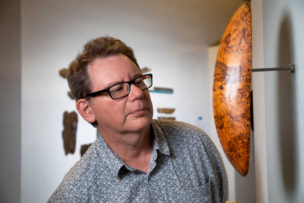 Curator Ian Coates examines a shield mounted on a wall.