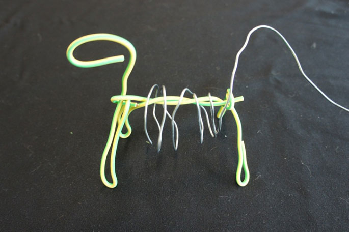 Electrical wire bent into the shape of a horse. Fencing wire is wrapped around the centre of the horse.