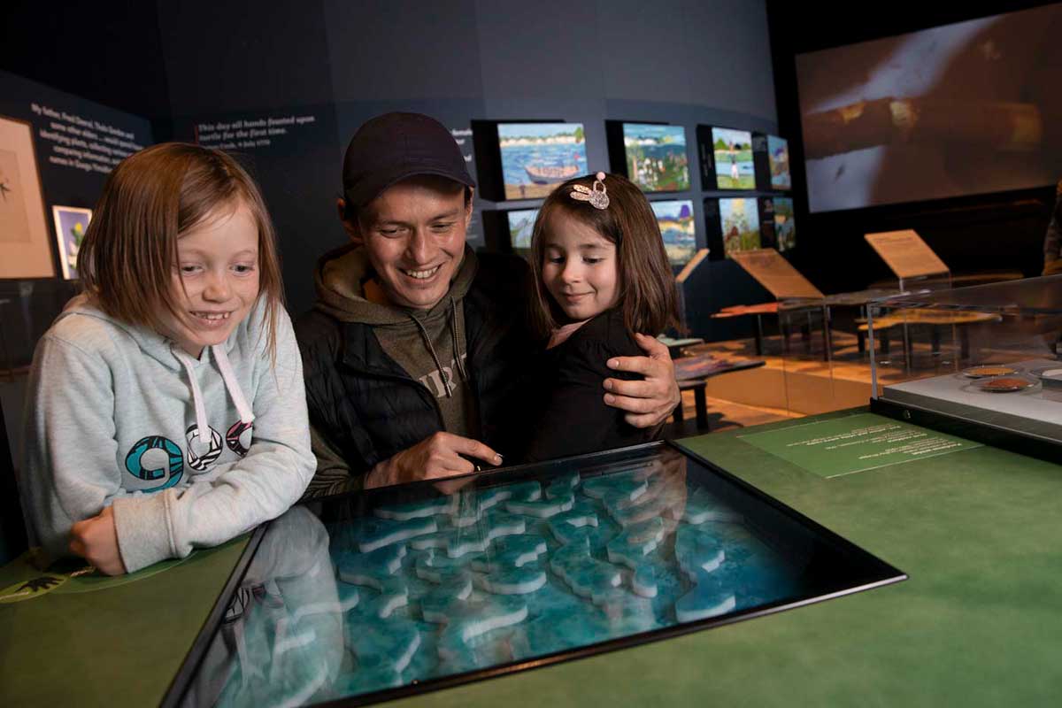 A man and two young girls behind a museum exhibit consisting of a blue-green reef puzzle. - click to view larger image