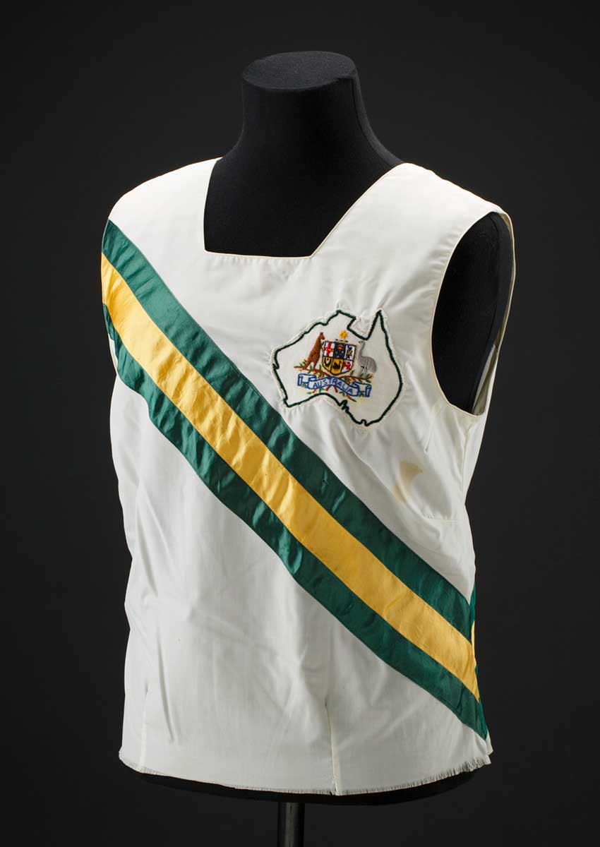 White singlet on a mannequin torso. The singlet has diagonal green and gold strips across the chest and the Australian coat of arms on the left breast. - click to view larger image