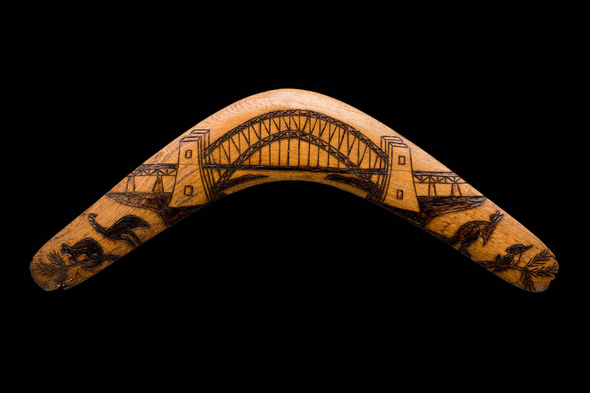 A symmetrical timber boomerang featuring, on the obverse, a pokerwork image of the Sydney Harbour Bridge, flanked on both sides by images of animals which include; (from left to right) a possum, an emu, a kangaroo and a kookaburra on a branch. - click to view larger image