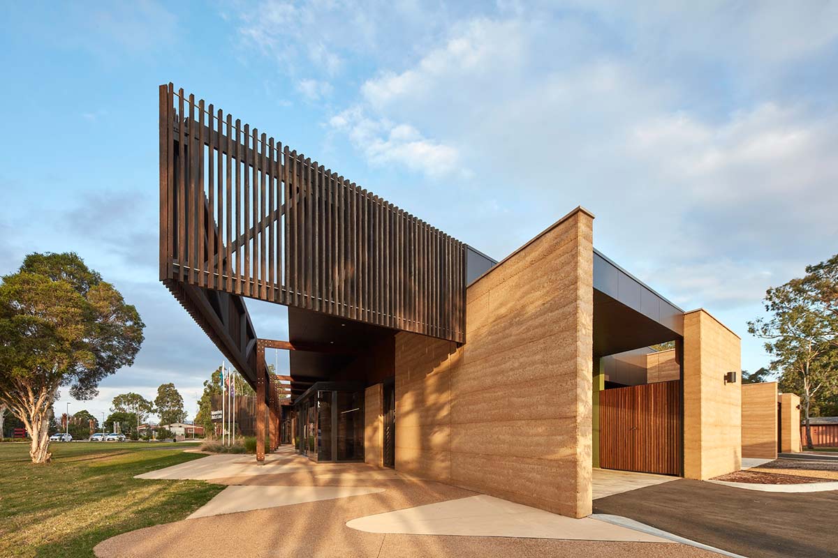 Promotional photograph of a contemporary style building with rammed earth walls, wood cladding and wooden slat features. - click to view larger image