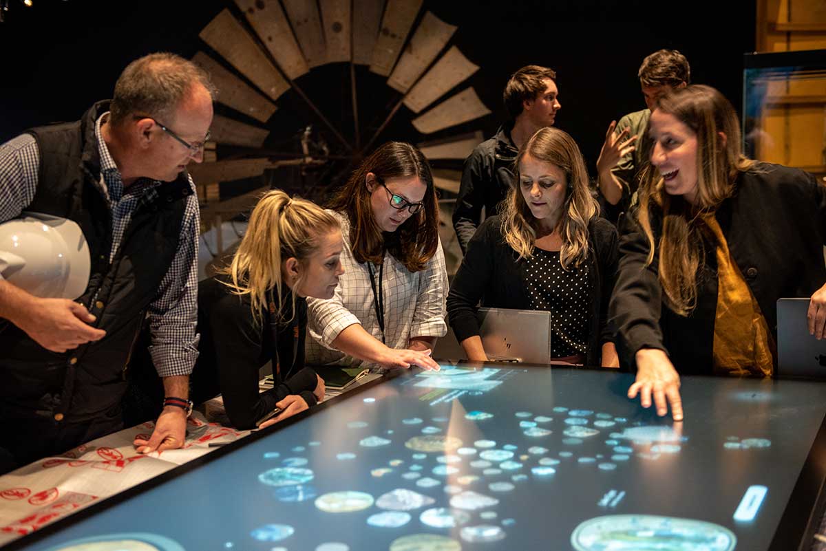 A group of men and women interact with an illuminated map.