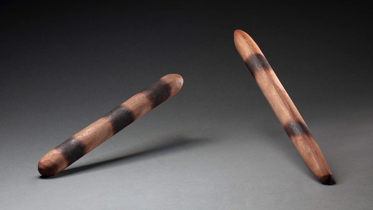 A pair of cylindrical, wooden clapsticks with tapered ends, and bands of dark brown on the surface of the wood. - click to view larger image