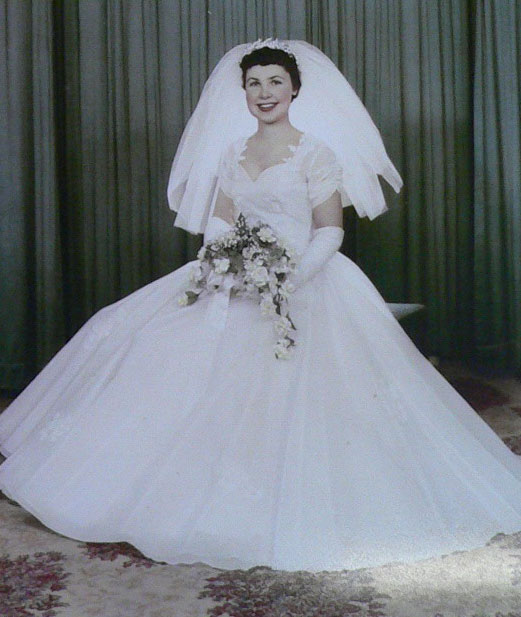 Portrait of a woman in a wedding dress and veil. She is holding a bouquet of flowers. - click to view larger image