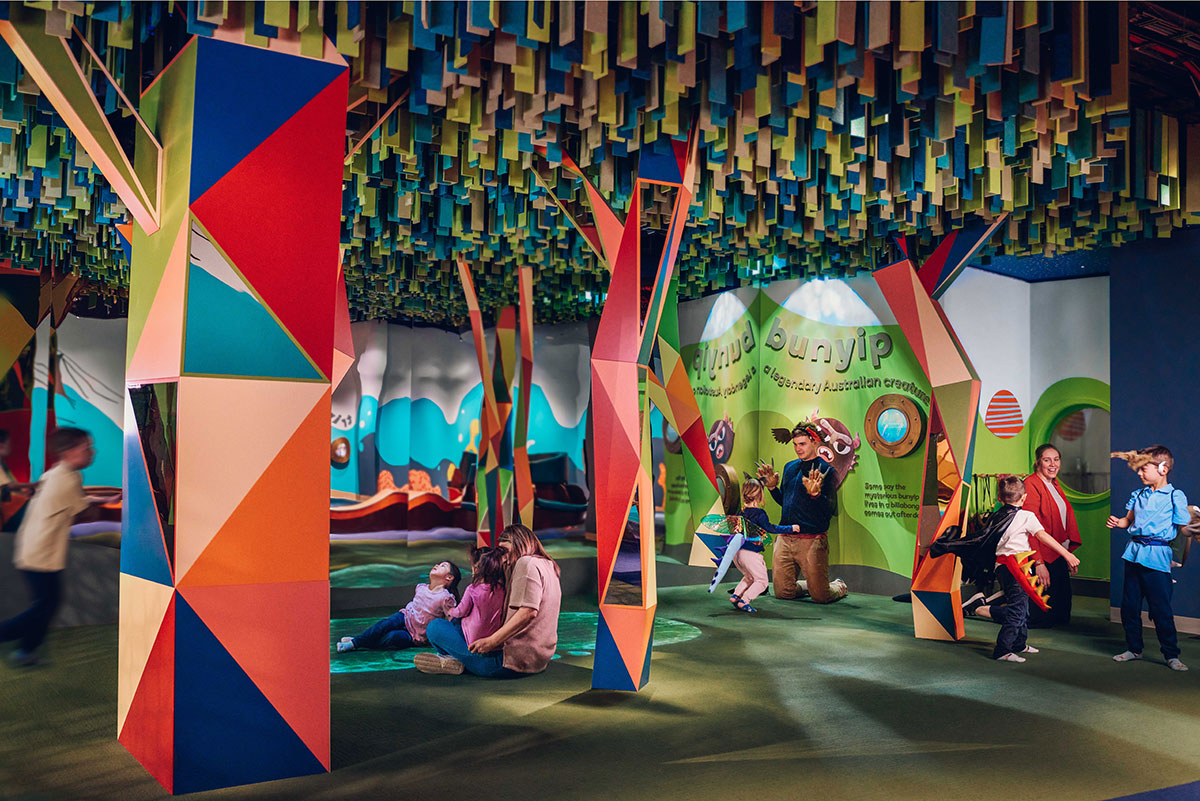 Children playing in a colourful recreational space, with geometric columns reaching to a textured roof.