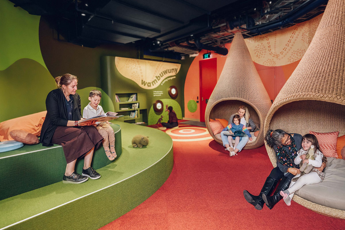 Children sitting with adults, reading, in a play space.