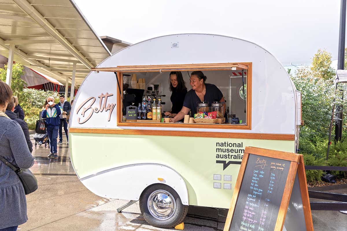 Two female baristas serving food and beverages from a small pink and green caravan. - click to view larger image