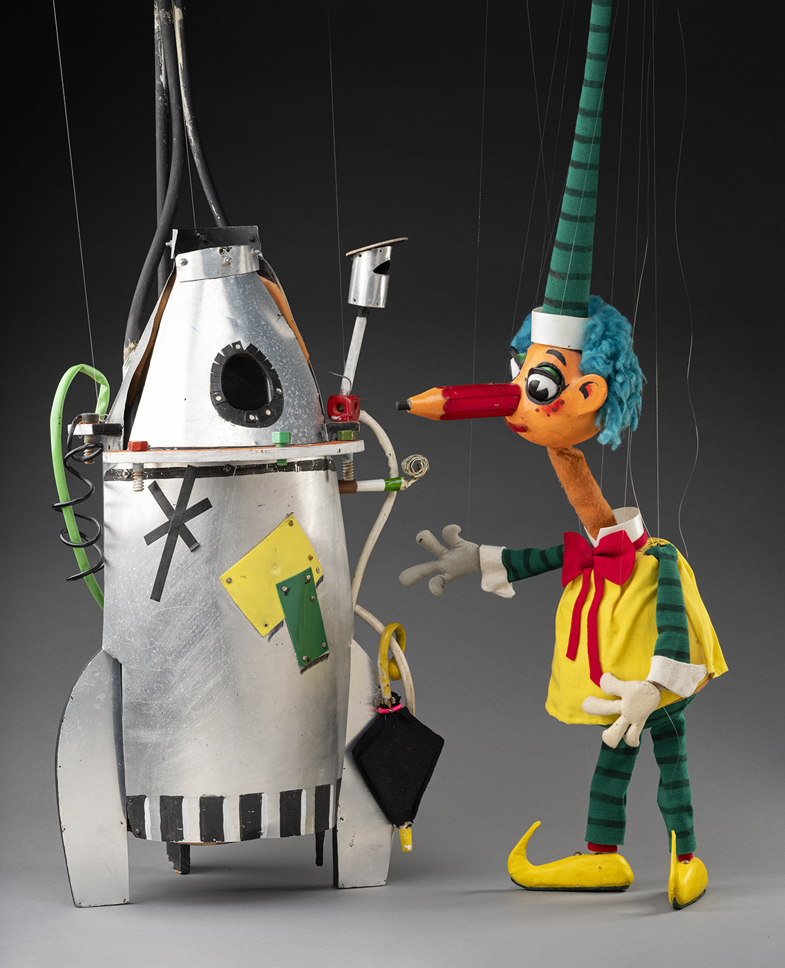 Mr Squiggle the puppet standing next to a silver rocket ship puppet. - click to view larger image