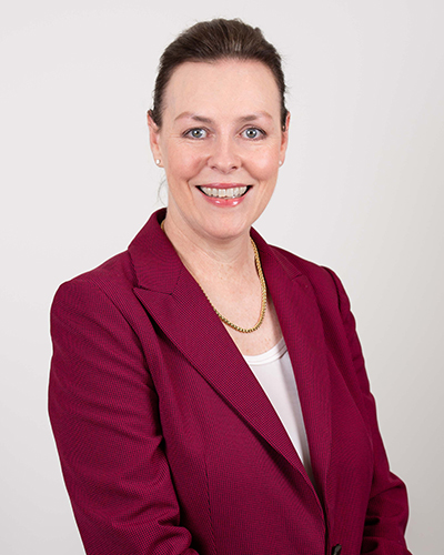 Photograph of Natasha Bowness. Natasha is wearing a maroon blazer and white top. She is smiling at the camera.