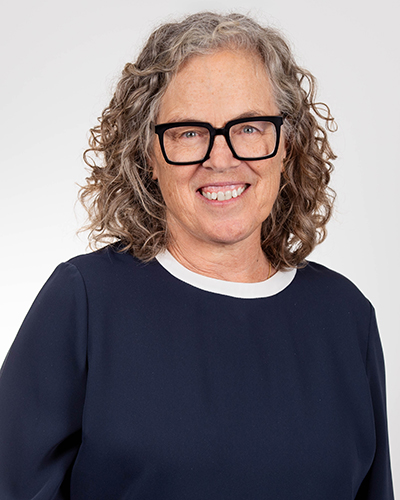 Studio portrait of Janine Freeman. Janine wears a dark blue top and glasses.