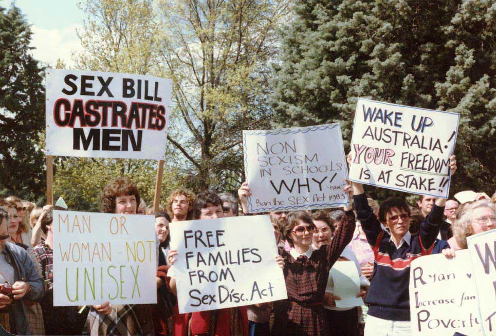 colour photo showing women and a couple of men protesting. Many are holding placards saying things like ‘Sex bill castrates men’, ‘Free families from Sex Disc Act’, ‘Wake up Australia! Your freedom is at stake’