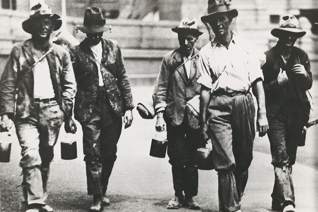 Four men and a woman walking abreast along the front of Old Parliament House.