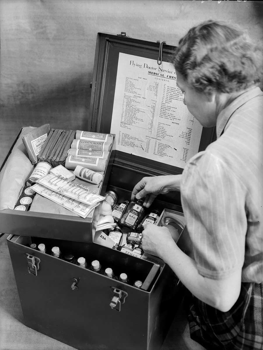 A woman sits on the floor examining the contents of a metal box.