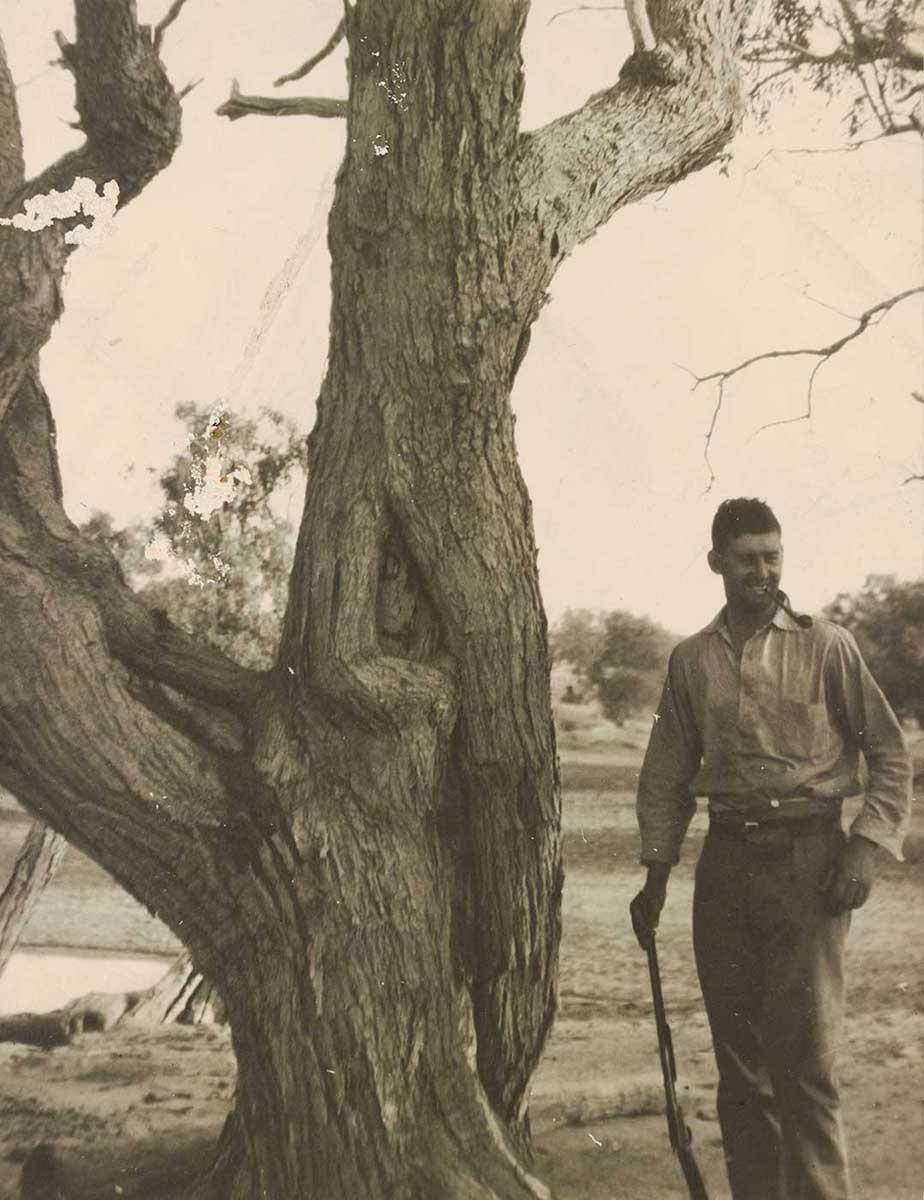 black and white photo showing tree with inscription and simple monument in background - click to view larger image