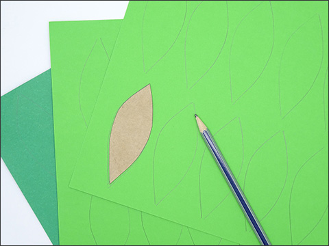 Two light green pieces of paper sit layered over a darker green piece of paper. There are leaf tracings on the top sheet with a led pencil placed on top.