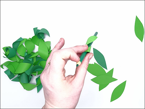 A hand holding a green pencil which is wrapped around with a small piece of green paper.