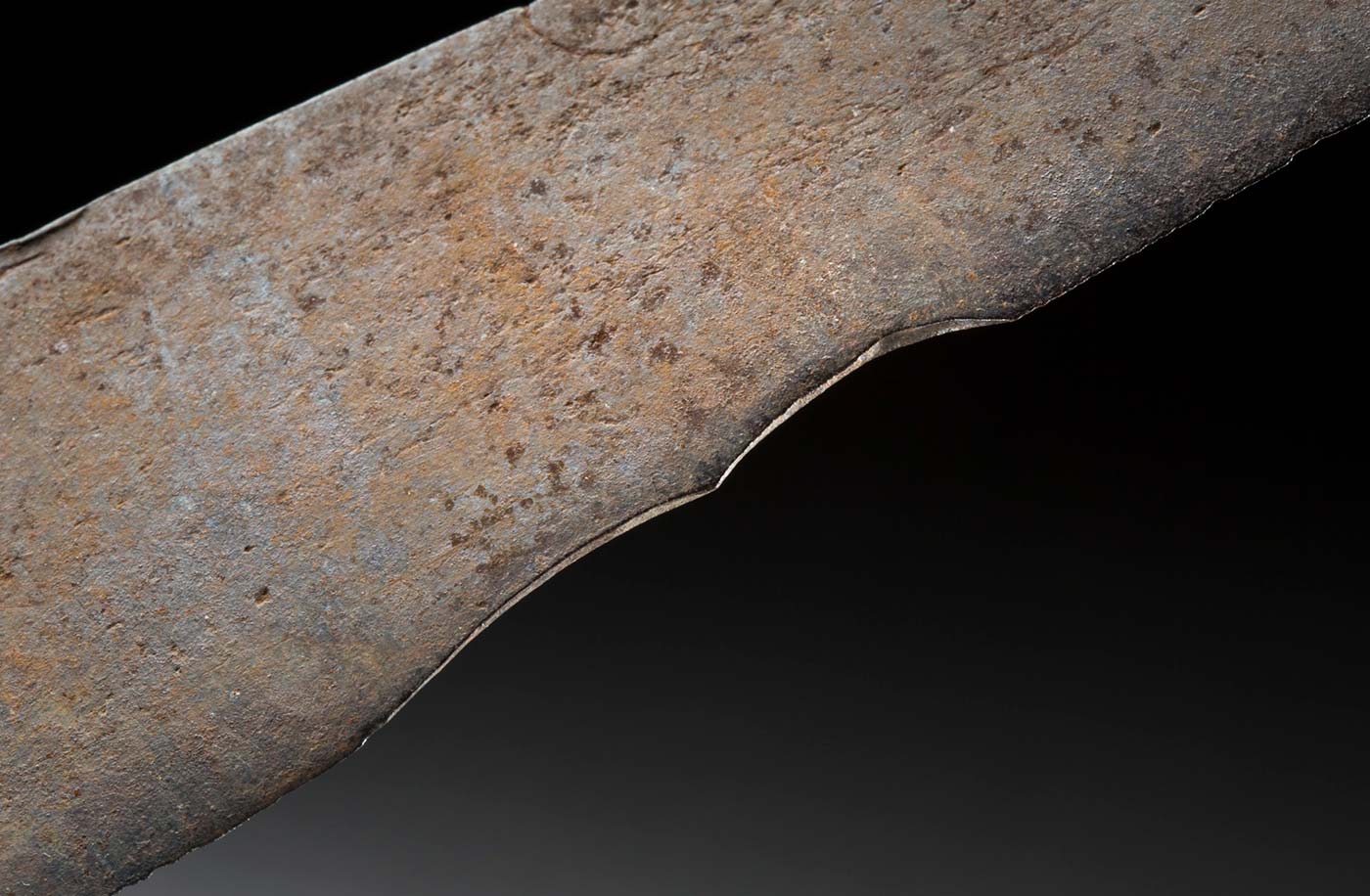 A knife with a rusted, shaped steel blade and bullock horn handle. The blade is held between two shaped pieces of grey-brown bullock horn and attached with metal studs. The blade has a straight top edge which is slightly thicker and a thinner curved cutting edge with nicks and scrapes from use. - click to view larger image