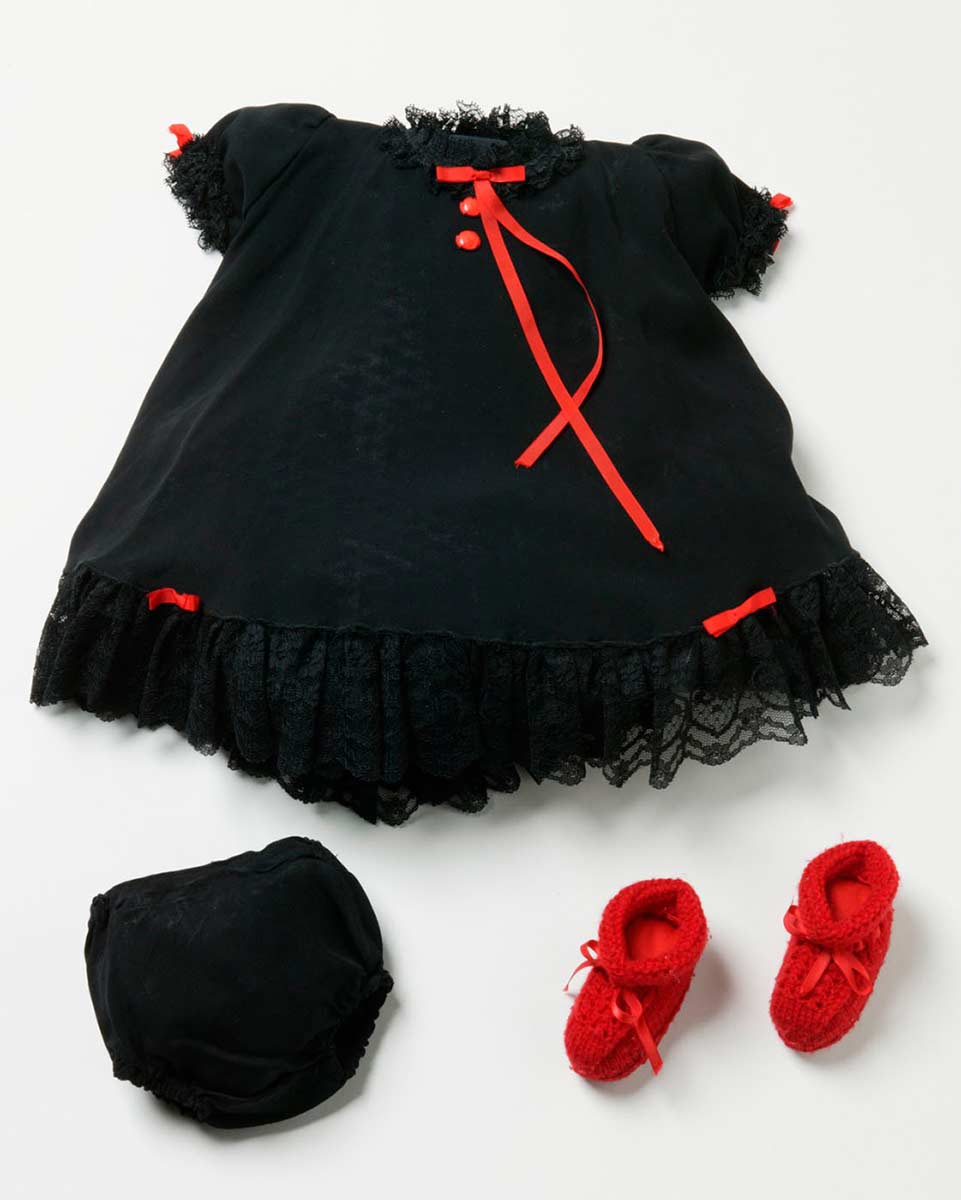 Small black dress with black lace trim at the neck, arms and bottom. Also has two thin red ribbon bows at the bottom and on the arms. Includes matching black bans and a pair of knitted red booties with red ribbon ties at the front. - click to view larger image