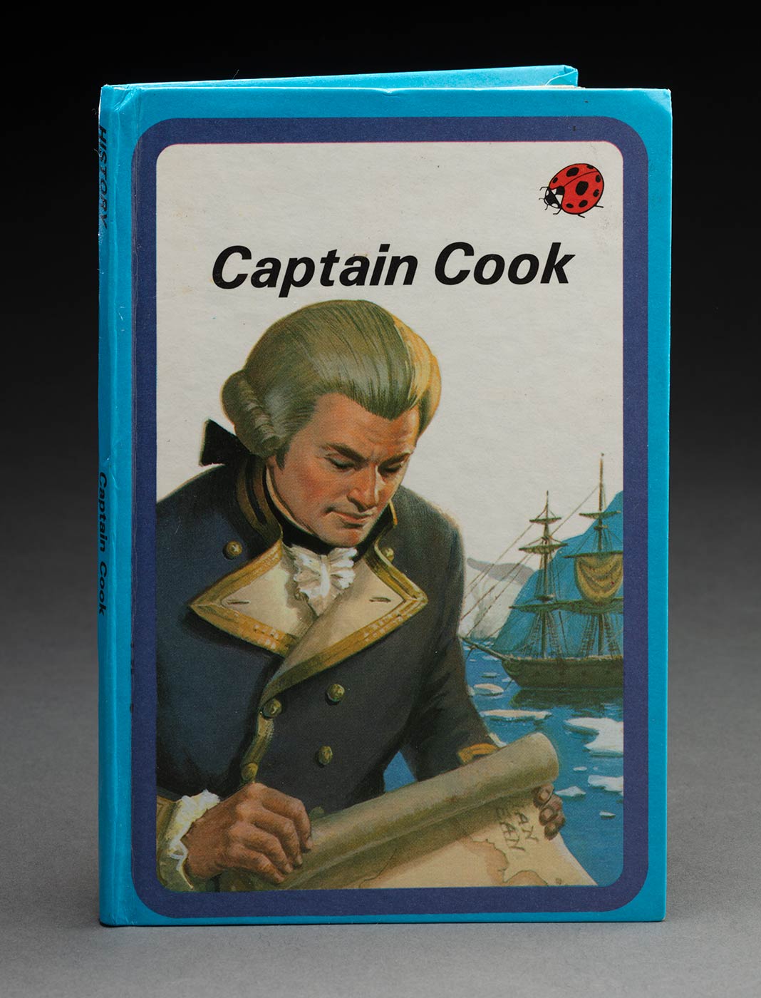 A hard cover book with the title 'Captain Cook'. The cover has a blue boarder and features a drawing of Captain Cook holding a map. - click to view larger image