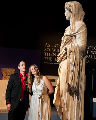 A man and woman look at a statue of a female form, on display in a museum.