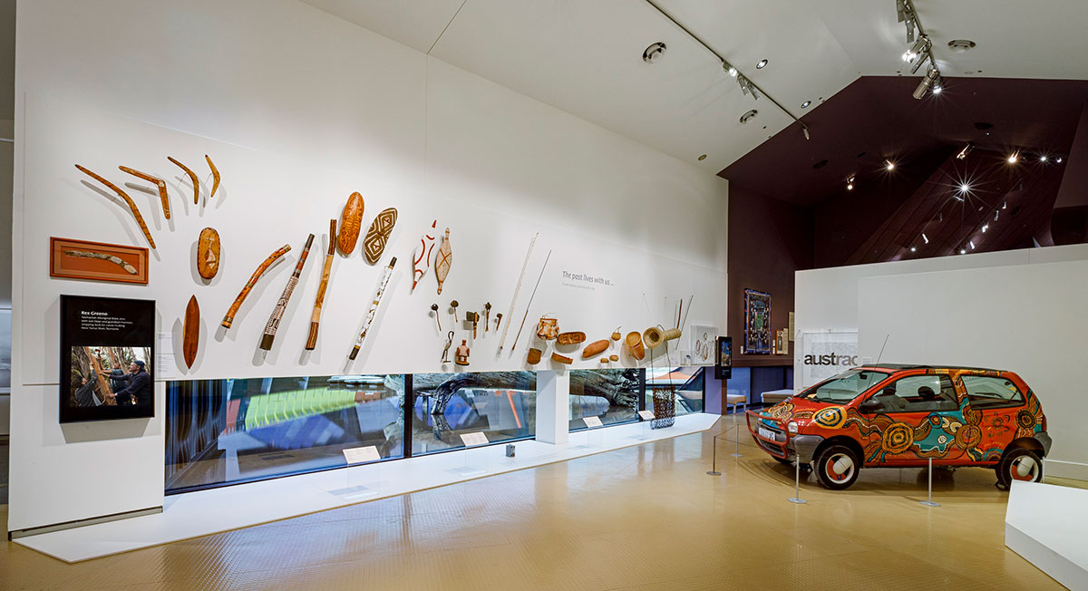 A view of a gallery space in a museum featuring various objects on display including an small car painted with dots and artefacts mounted on the wall.