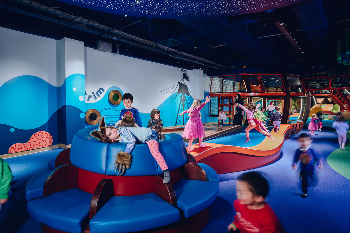 Children playing in a colourful recreational area, with a central wave feature.